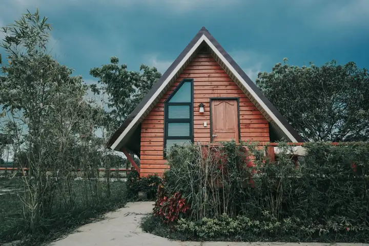 A wooden A-frame tiny house surrounded by plants