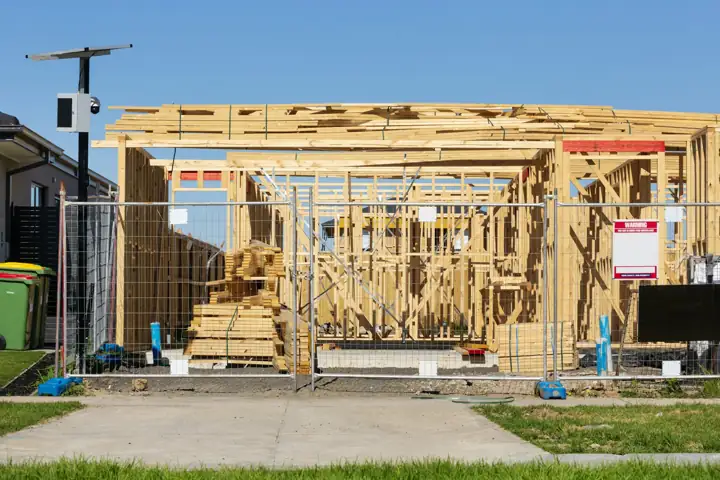 A wooden house frame going up behind a construction fence