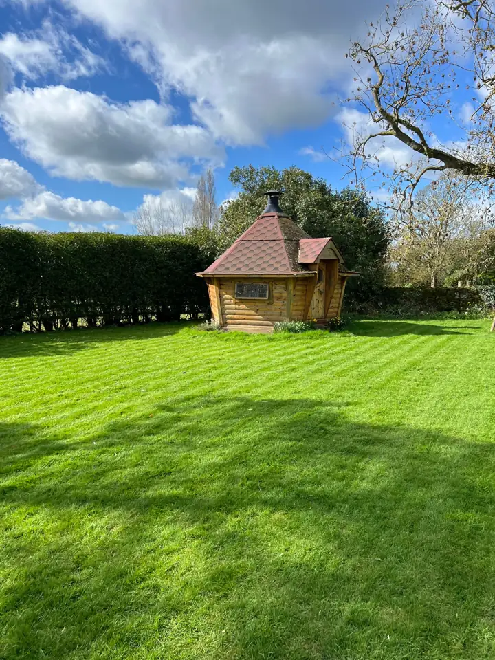 A small wooden hut at the edge of a green backyard lawn under a blue sky