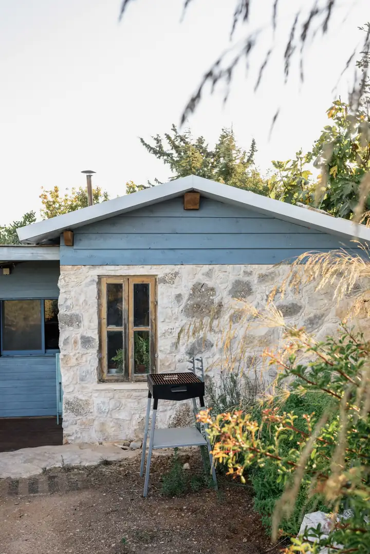 A small stone cottage with a grill and a green yard
